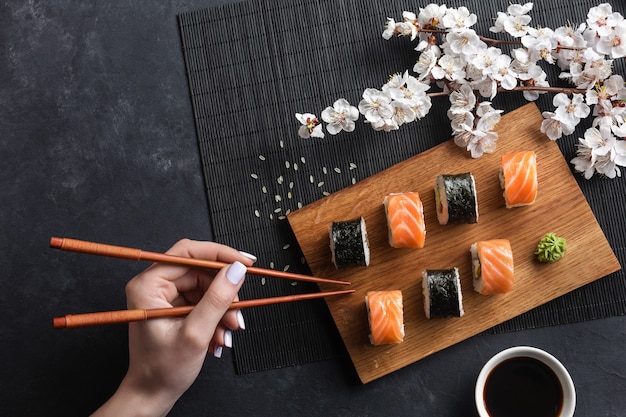 Conjunto de sushi, maki rolls, mano con palillos y rama de flores blancas en la mesa de piedra. Vista superior.