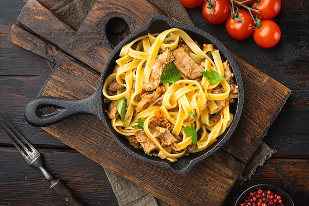 Conjunto de tagliatelle de estofado de conejo, en sartén o olla de hierro fundido, en la vieja mesa de madera oscura, vista superior plana