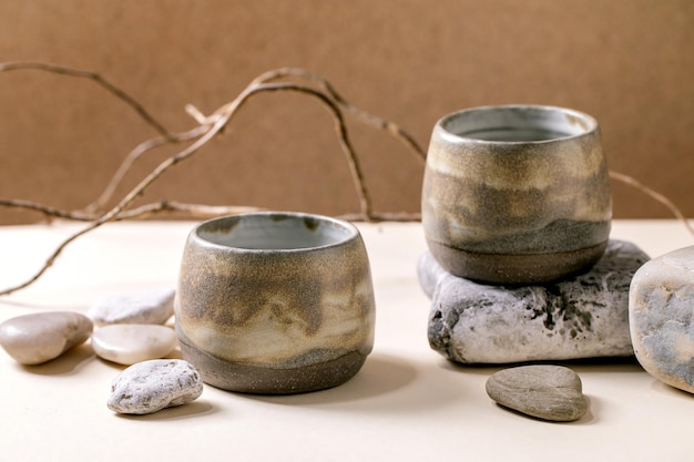 Conjunto de tazas de cerámica artesanales de textura gris vacía con rama seca y piedras de pie sobre la mesa Espacio de copia de pared marrón