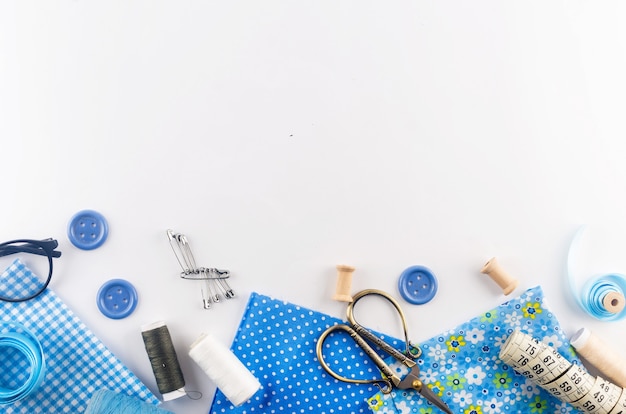 Conjunto de telas de hilo de coser azul, botones y accesorios sobre un fondo blanco. Composición plana con otras cosas de costura.