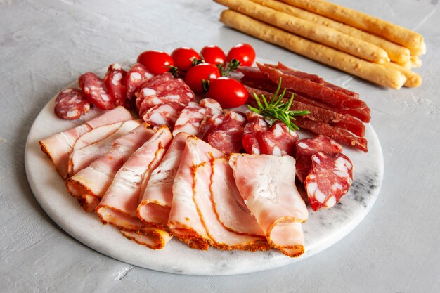 Conjunto de tocino ahumado, salami y basturma servido con pitomatoes y pan grissini,