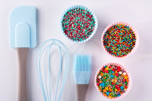 Conjunto de utensilios de cocina para cocinar pasteles y chispas de arco iris para decoración sobre fondo blanco.