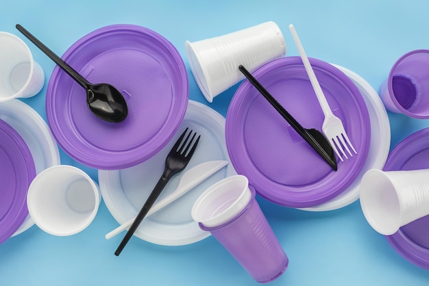 Un conjunto de utensilios de plástico desechables, lilas y blancos. Fondo azul, copie el espacio.