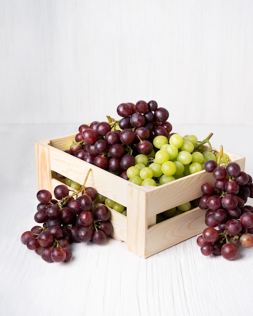 Conjunto de uvas jugosas orgánicas naturales, frutos rojos y verdes en caja de madera, sobre fondo blanco.