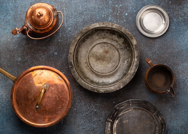 Conjunto de vajilla vacía de cobre y alpaca de época antigua sobre fondo de hormigón rústico. Utensilios antiguos: sartén, platos, cuencos, tetera. Vista superior de hermosos utensilios de cocina retro envejecidos del mercado de pulgas