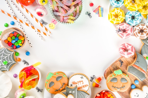 Conjunto de varios dulces clásicos de Halloween sobre fondo blanco. Selección surtido de galletas tradicionales, pan de jengibre, golosinas, dulces y decoración de calabazas. Concepto de truco o trato, espacio de copia de vista superior