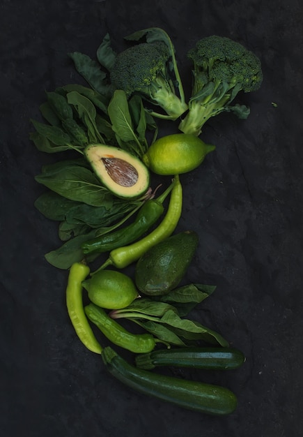 Conjunto de vegetales verdes crudos. Brócoli, aguacate, pimiento, espinacas, zuccini y lima sobre piedra oscura.