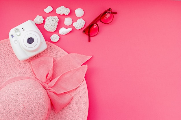 Conjunto de verano de una cámara, gafas, sombreros y corales sobre un fondo rosa