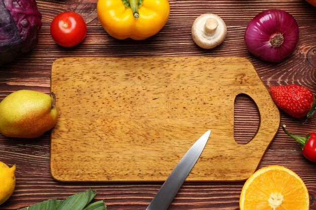 Conjunto de verduras y frutas frescas con tabla de cortar sobre fondo de madera