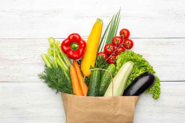 Conjunto de verduras y hierbas en una bolsa de papel sobre un fondo de madera blanca. Comida vegetariana saludable.