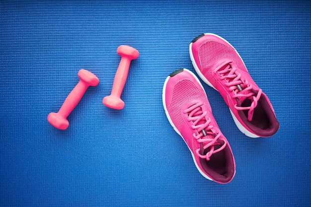 Conjunto de zapatillas de deporte y pesas de color rosa sobre fondo azul, vista superior