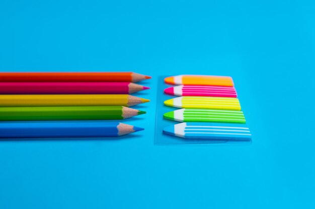 Conjuntos de lápis brilhantes em amarelo, laranja, rosa, verde, azul na cor de adesivos em forma de lápis em um azul. Fechar-se.