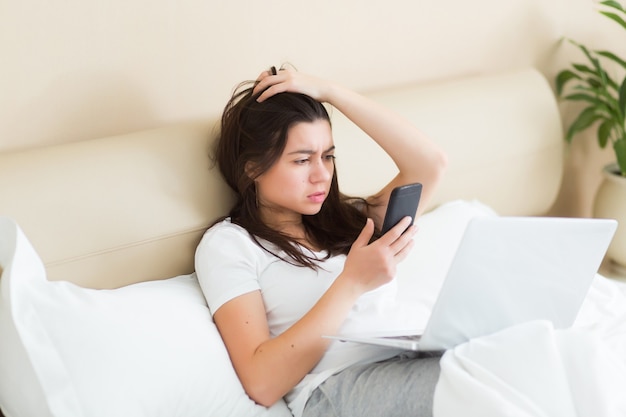 Conmocionada y angustiada joven mirando el teléfono celular en casa