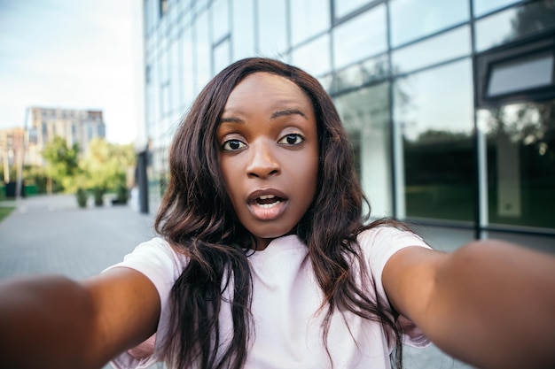 Conmocionada mujer afroamericana de pie fuera tomando selfie