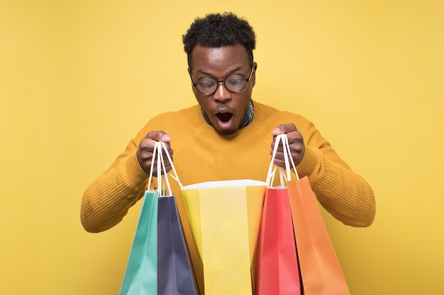 Conmocionado joven africano sosteniendo bolsas de compras siendo sorpresas