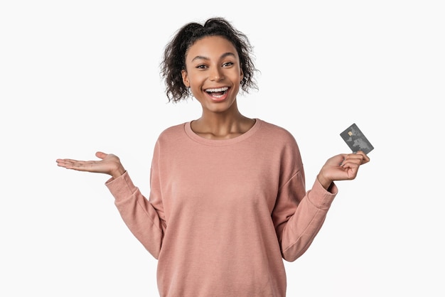 Conmocionado joven afroamericana con tarjeta de crédito en la mano aislado sobre fondo blanco.