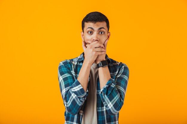 Foto conmocionado joven vestido con camisa a cuadros que se encuentran aisladas sobre la pared naranja, cubren la cara