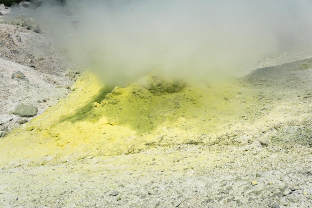 Cono amarillo de azufre cristalizado alrededor de una solfatara humeante en la ladera de un volcán