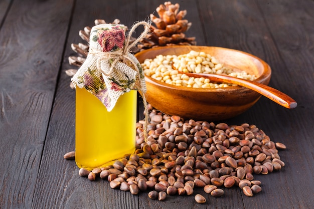 Cono de cedro con nueces y una botella de vidrio con aceite en madera.