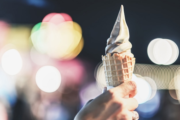 Foto cono de crema suave del helado sabroso en la mano femenina que se sostiene con la luz brillante hermosa borrosa del bokeh