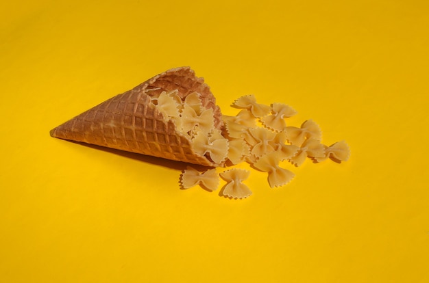 Cono de galleta de helado con arcos de pasta sobre fondo amarillo brillante