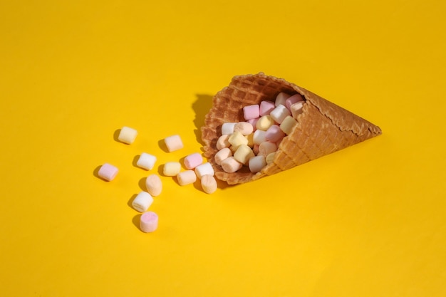 Cono de galleta de helado con malvaviscos sobre fondo amarillo con sombra profunda