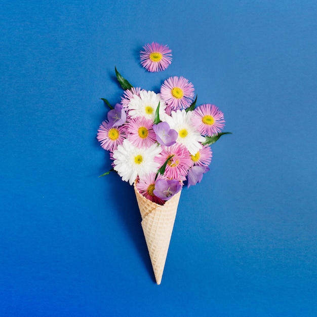 Cono de galleta con ramo de flores de manzanilla sobre fondo azul. Endecha plana, vista superior