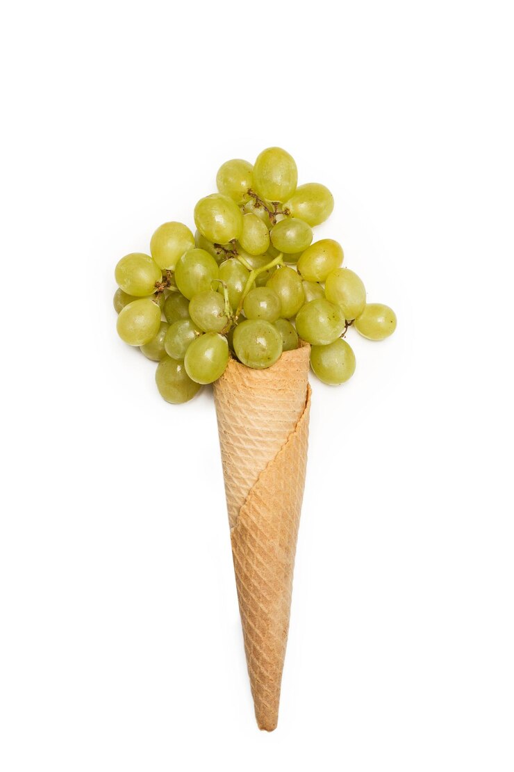Foto un cono de galleta con uvas verdes sobre un fondo blanco.