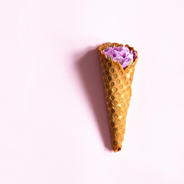 Foto un cono de gofre con flores moradas sobre un fondo rosa.