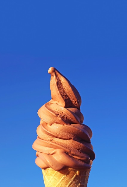Cono de helado de chocolate suave contra el soleado cielo azul vibrante