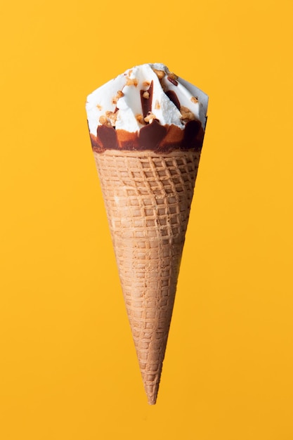 Foto cono de helado de crema con avellanas y almendras sobre un fondo amarillo-naranja