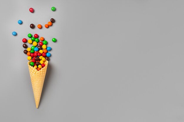 Cono de helado con dulces multicolores sobre fondo gris