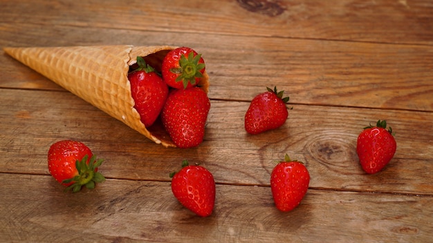 Cono de helado con fresas sobre un fondo de madera. Frutos rojos en un cono de galleta. Foto de verano