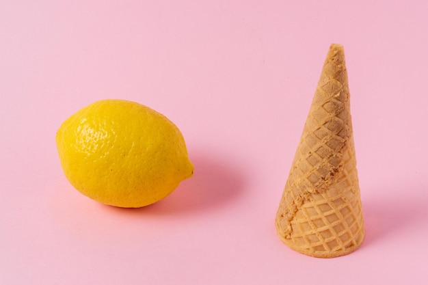 Cono de helado y fruta de limón sobre un fondo rosa claro.