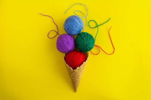 Foto cono de helado con hilos de colores para tejer en el centro de la mesa amarilla. vista superior. copie el espacio.