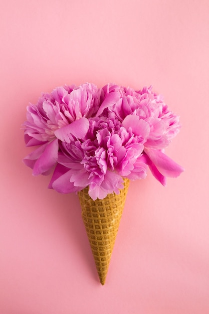 Cono de helado con peonías rosas en el centro del fondo rosa