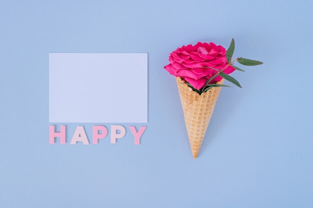 Cono de helado plano de la endecha con la rosa del rosa en el blanco claro azul y blanco. Texto feliz