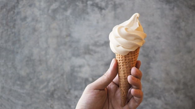 Cono de helado de servicio suave en la mano con fondo de cemento.