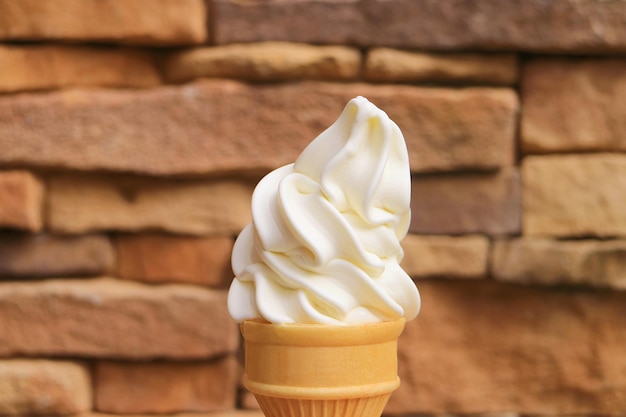 Cono de helado suave de vainilla con pared bloqueada de piedra borrosa en el fondo