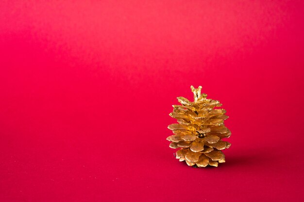 Foto cono de pino dorado sobre un rojo, adornos navideños.