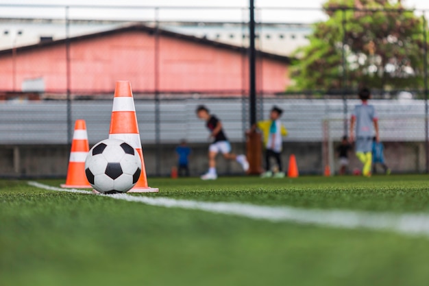 Cono de tácticas de balón de fútbol en campo de hierba con antecedentes de formación Formación de niños en fútbol