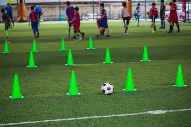 Cono de tácticas de balón de fútbol en campo de hierba con antecedentes de formación Formación de niños en fútbol