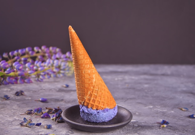 Cono de waffle con helado lila morado en el gris oscuro