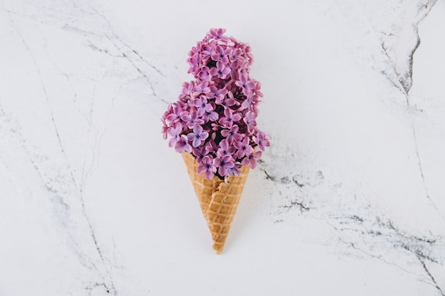 Cono de waffle con ramo de flores lilas sobre fondo de mármol