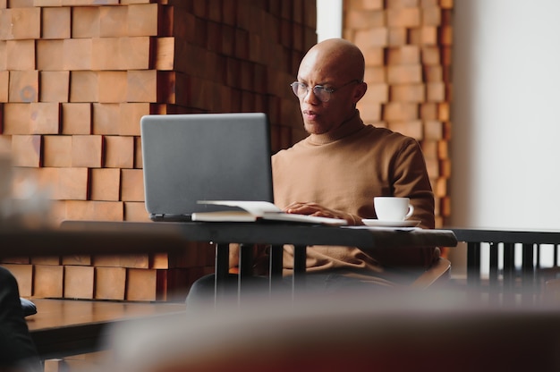 Conocimiento, aprendizaje, educación y tecnología. Un estudiante de hardowrking vestido informalmente con peinado afro que resuelve problemas matemáticos, sentado en la mesa de café con libros de texto y dispositivo electrónico