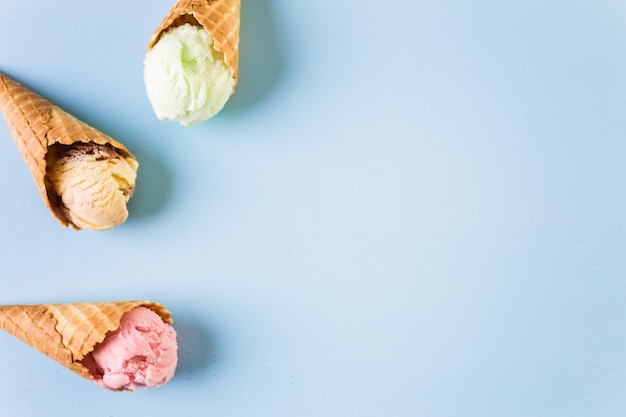 Conos de helado de galleta con bolas de helado sobre un fondo azul.