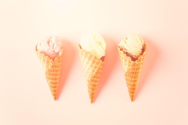 Conos de helado de gofre con plato de bolas de helado sobre un fondo rosa.