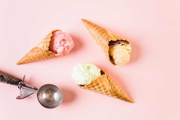 Conos de helado de gofre con plato de bolas de helado sobre un fondo rosa.