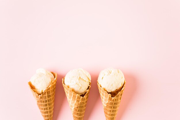 Conos de helado de gofre con plato de bolas de helado sobre un fondo rosa.