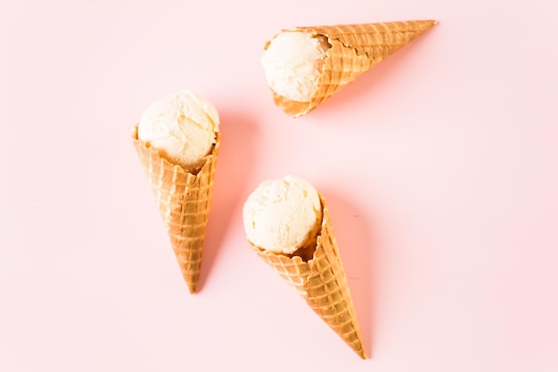 Conos de helado de gofre con plato de bolas de helado sobre un fondo rosa.